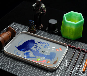 On the miniature painting station are placed a wet palette, a brush cleaning jar, a handle, and a miniature figure.