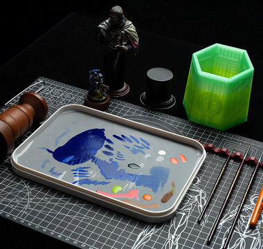 On the miniature painting station are placed a wet palette, a brush cleaning jar, a handle, and a miniature figure.