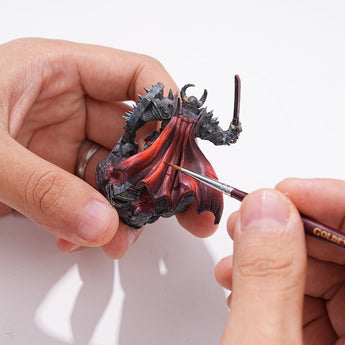 Fine detail paint brush applying highlights to the red cape of a fantasy miniature figurine.