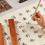 Chinese Calligraphy Brush with natural bristles, writing characters on textured paper, alongside a wooden brush rest.