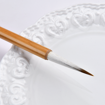 Chinese Calligraphy Brush, natural white bristles with brown tip, bamboo handle, on a white ceramic palette.