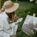 Professional Artist using a nylon travel brush, plastic palette with vibrant acrylic paint, creating art outdoors.