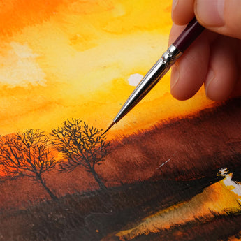 Artist using a Miniature Detail Brush to paint fine trees on a vibrant watercolor sunset landscape painting.