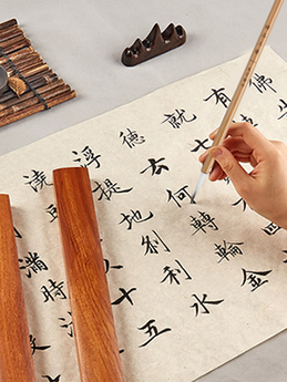 Chinese Calligraphy Brush with natural bristles, writing characters on textured paper, alongside a wooden brush rest.